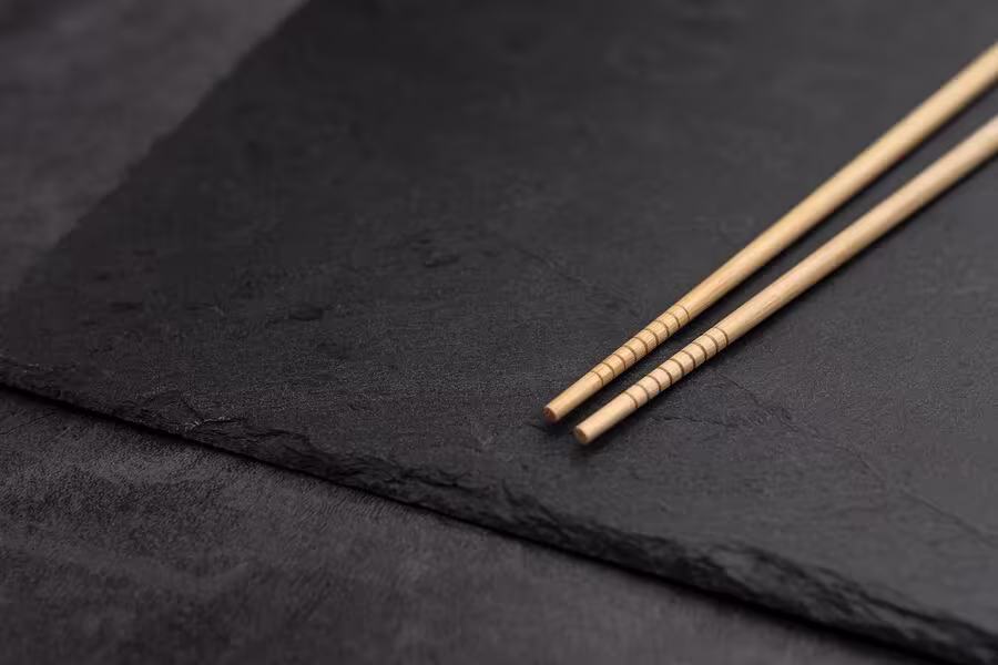 A pair of wooden chopsticks rests on a dark, textured slate surface.