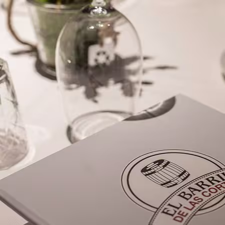 Mesa impecable en El Barril de las Cortes con cristalería elegante, detalles cuidados y su menú, perfecto para una experiencia única.