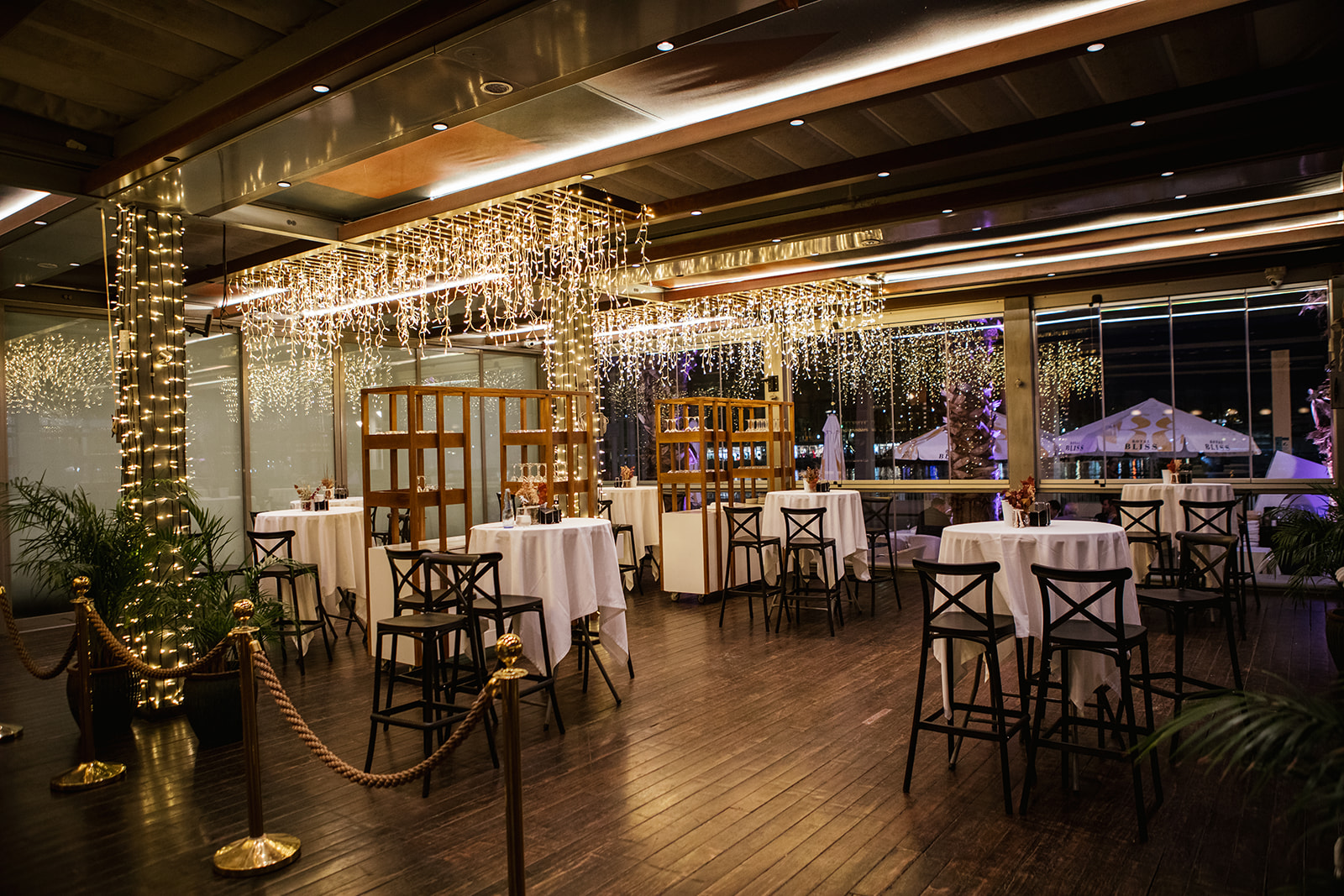 Kaleido Málaga Port destaca por su elegante decoración con luces colgantes y mesas redondas, ideal para cenas y eventos exclusivos junto al puerto.