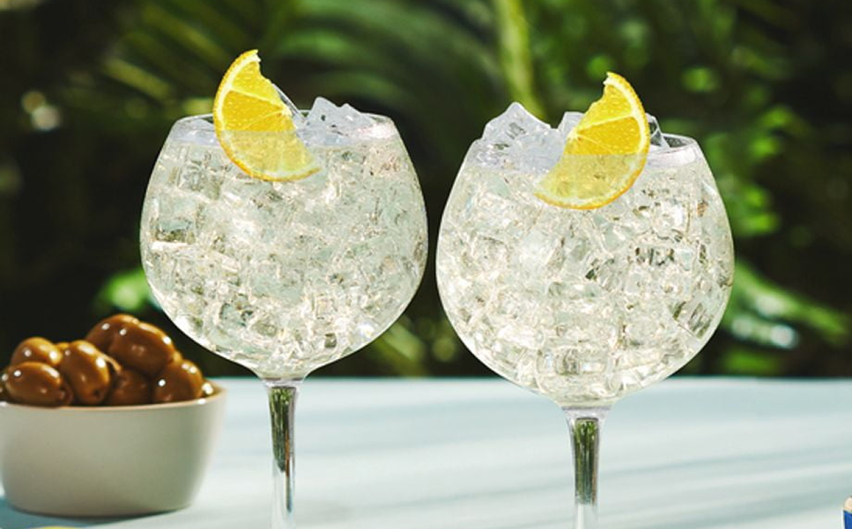 Two gin and tonics garnished with lemon slices, served in balloon glasses on a sunlit table