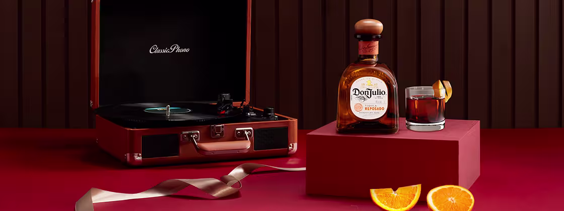 Don Julio Reposado bottle beside a cocktail glass and a suitcase vinyl record player