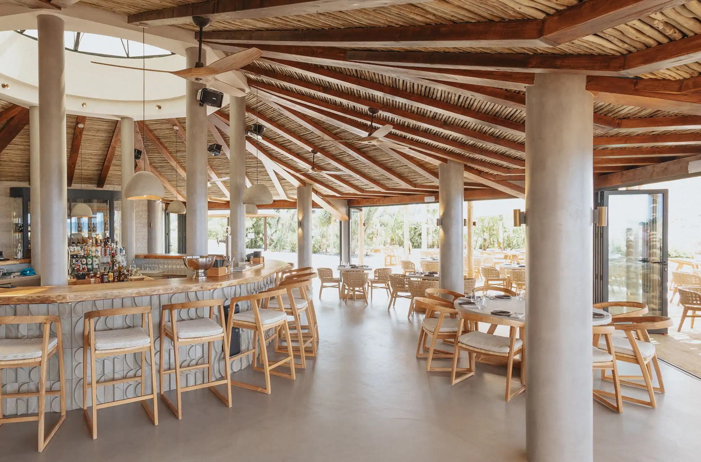 Dune Beach destaca con su techo de madera rústica, columnas modernas y mobiliario ligero, creando un ambiente cálido y playero.
