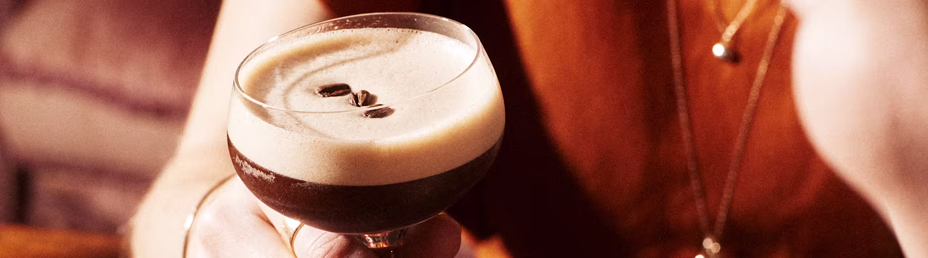 Close-up of an Espresso Martini in a coupe glass, held in a warmly lit, intimate setting