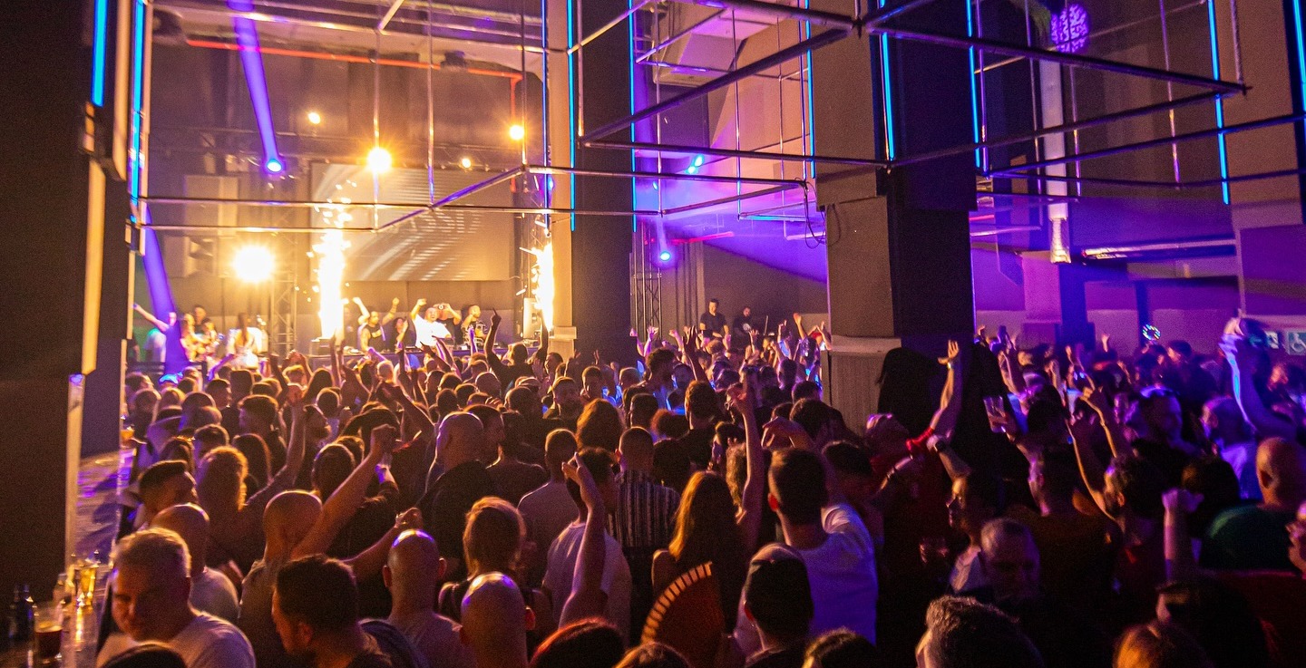 Ambiente vibrante en Art Club, con una multitud disfrutando bajo luces de neón y un escenario iluminado en una sala de diseño moderno.