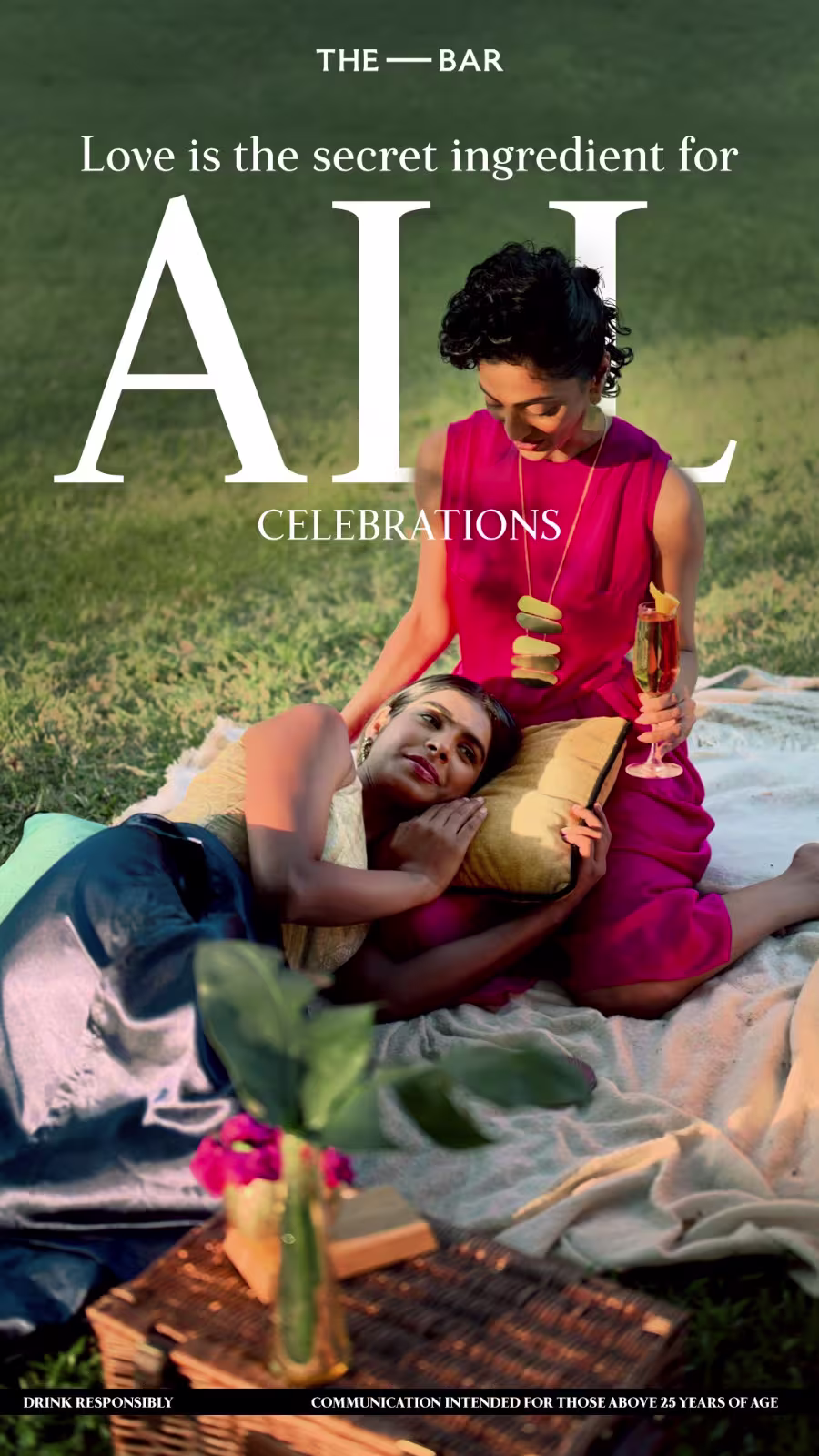 Two women relax on a picnic blanket outdoors, with one lying down and the other sitting up holding a drink, surrounded by cushions and flowers. Text reads: Love is the secret ingredient for all celebrations.