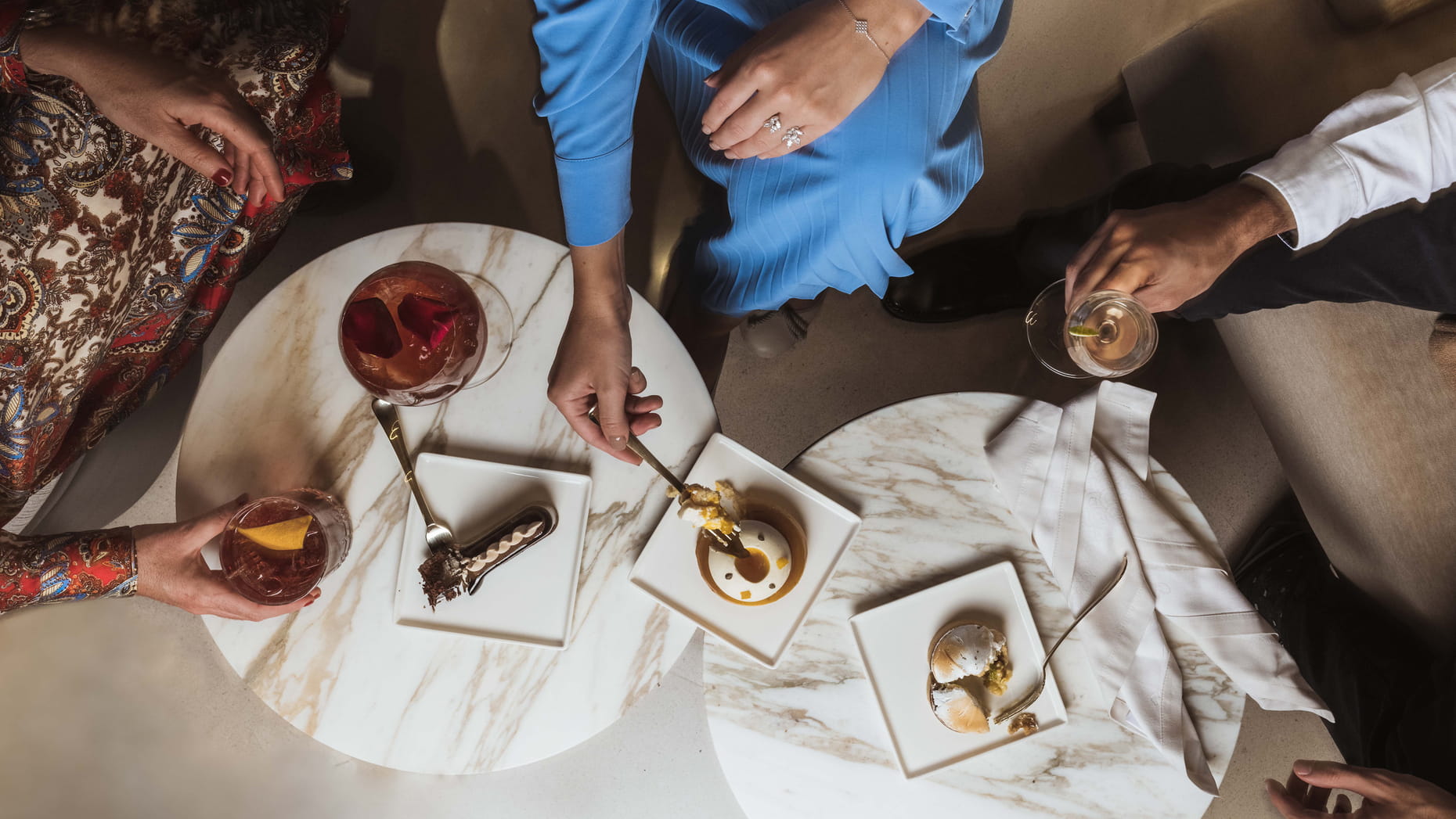 Postres y cócteles en El Patio del Hotel Four Seasons, presentados sobre mesas de mármol, en un ambiente sofisticado y acogedor.