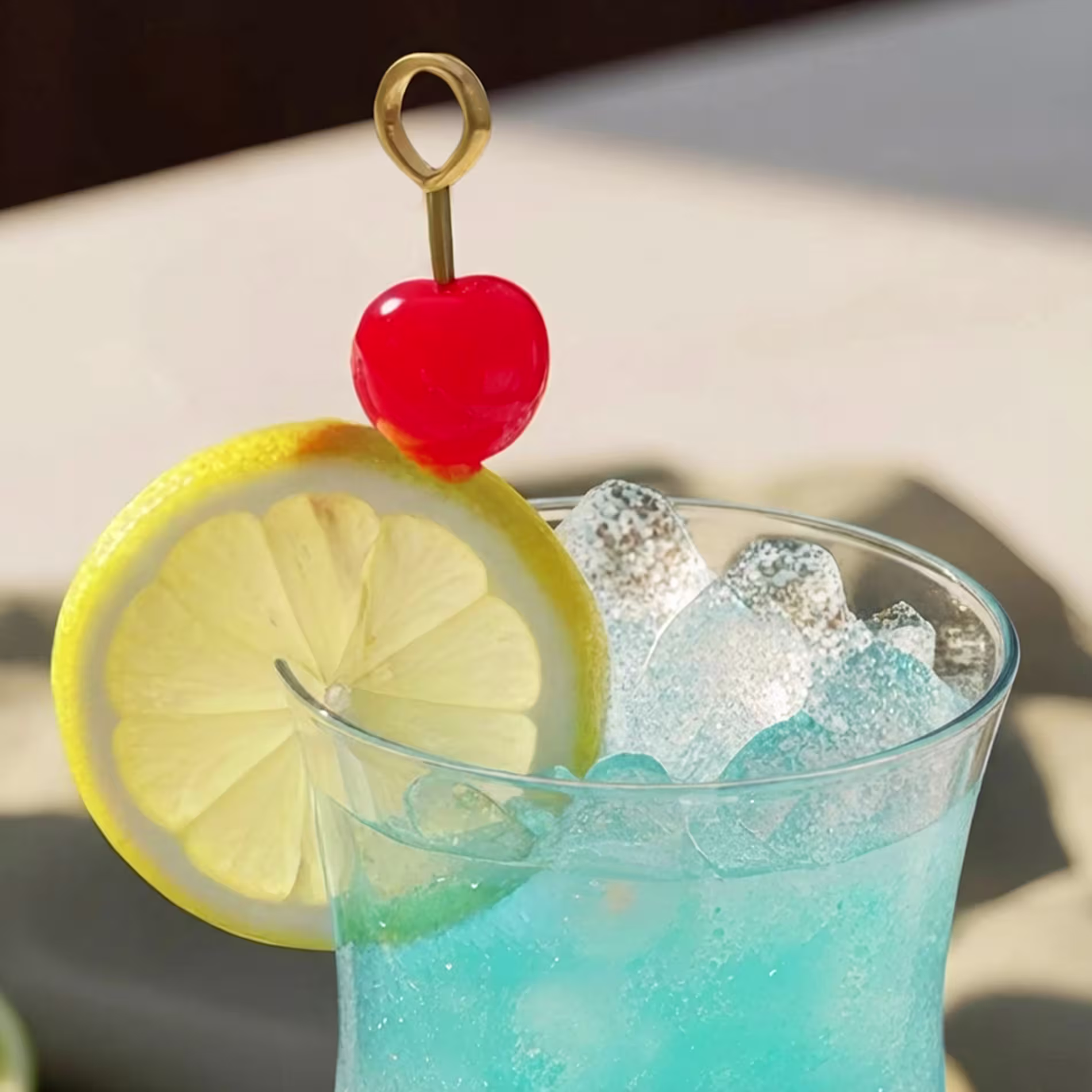 A lemon slice and glacé cherry garnish a Blue Lagoon cocktail.