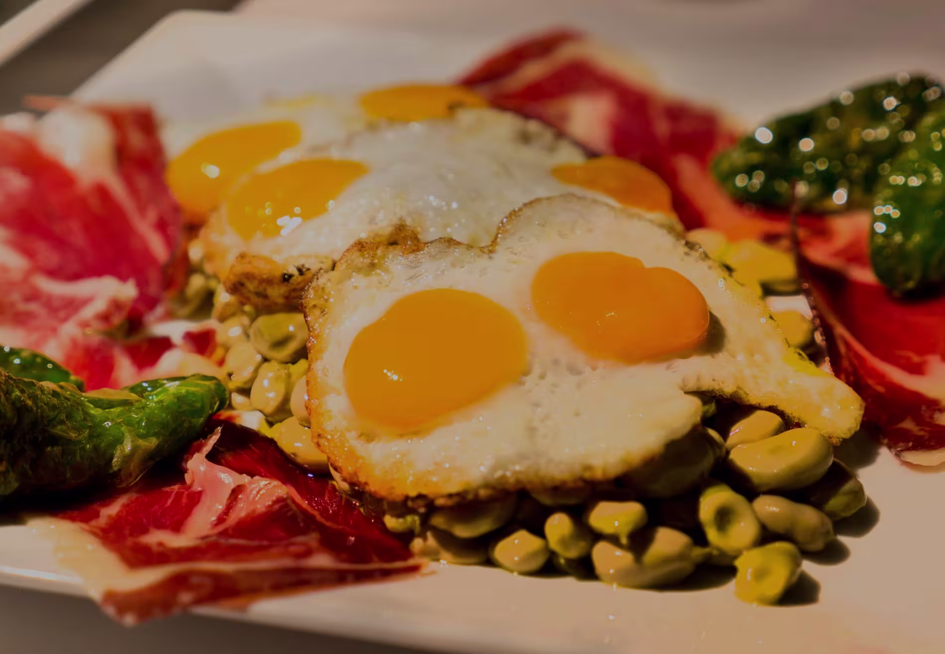 Huevos fritos con yema dorada acompañados de jamón ibérico, habas frescas y pimientos verdes en Bienmesabe Arturo Soria.