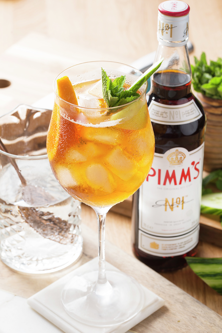Close-up of Pimms cocktail with ice and mint in a wine glass next to a bottle of Pimms No.1