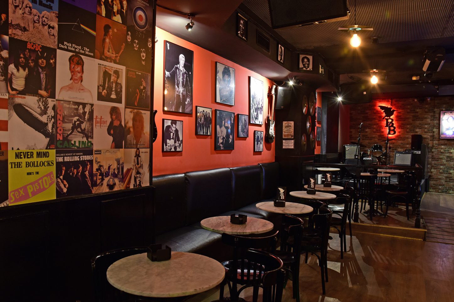 La foto muestra el interior de BlackBird.. Hay varias mesas y sillas dispuestas para los clientes, y las paredes están adornadas con varios carteles y fotos, predominantemente de bandas de música y figuras icónicas de la cultura pop.