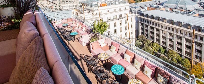 Terraza de Casa Suecia, con sofás rosados, mesas decorativas y vistas panorámicas de Madrid bajo un cielo despejado.
