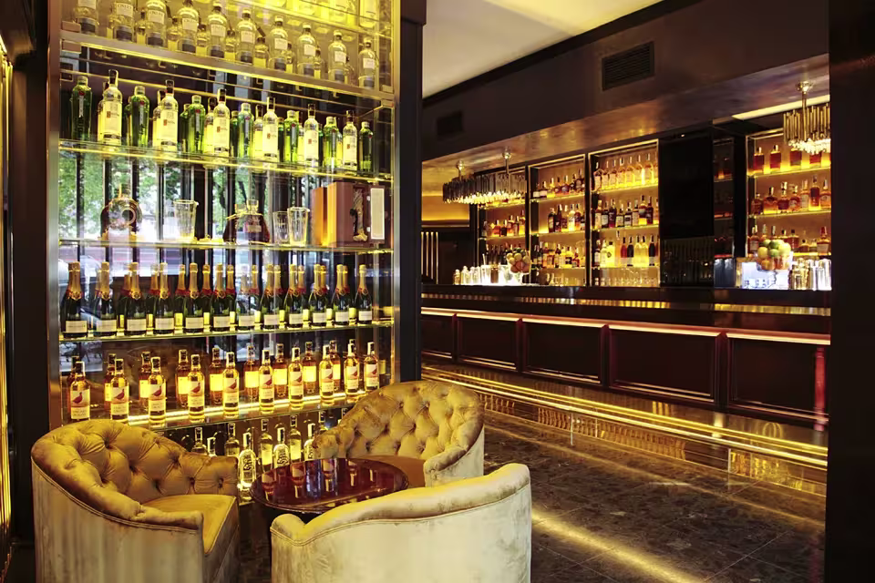Solange Cocktails destaca con su barra iluminada y estantes repletos de bebidas premium, ofreciendo un ambiente sofisticado con asientos elegantes.