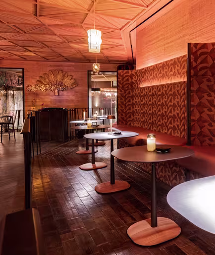 La imagen muestra el espacio interior del restaurante Lady Bongo, con un mural vibrante y colorido en la pared. El mural presenta varios motivos florales y animales, creando un tapiz intrincado de formas y colores. Hay mesas con sillas frente al mural