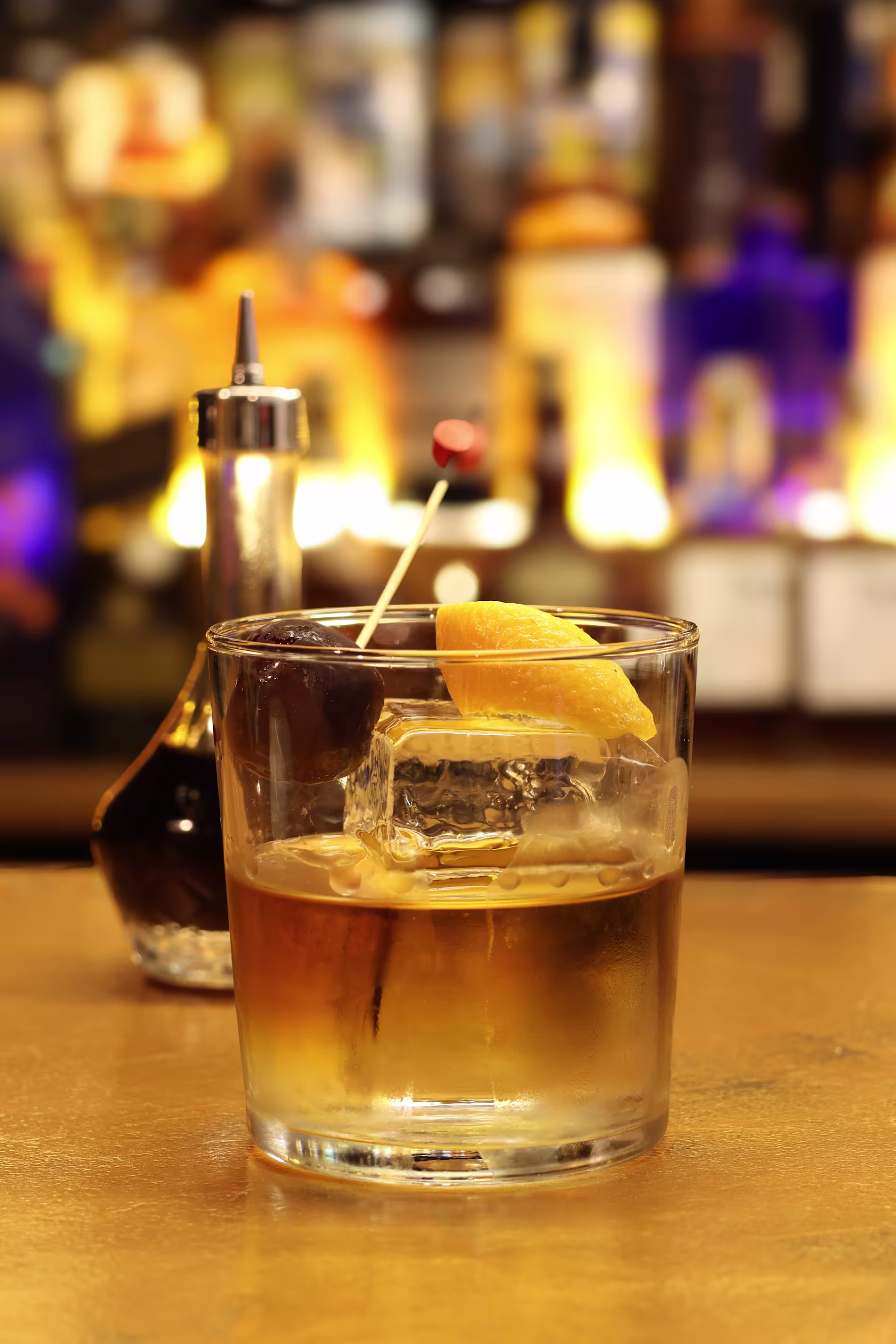 La foto muestra el espacio interior de Holy drop whisky Club, con iluminación tenue. El punto focal es una gran estantería iluminada llena de varias botellas, predominantemente de licores, debido a sus formas y la manera en que están dispuestas.