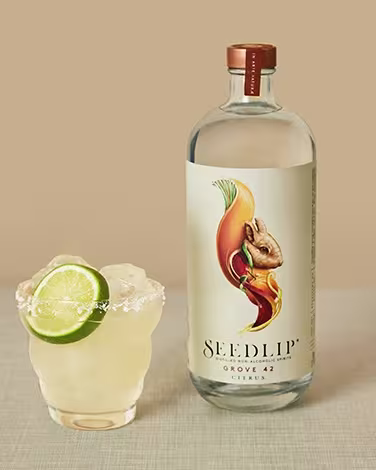 A non-alcoholic margarita in a rocks glass with a salt rim and a lime wheel garnish, next to a bottle of Seedlip Grove 42.