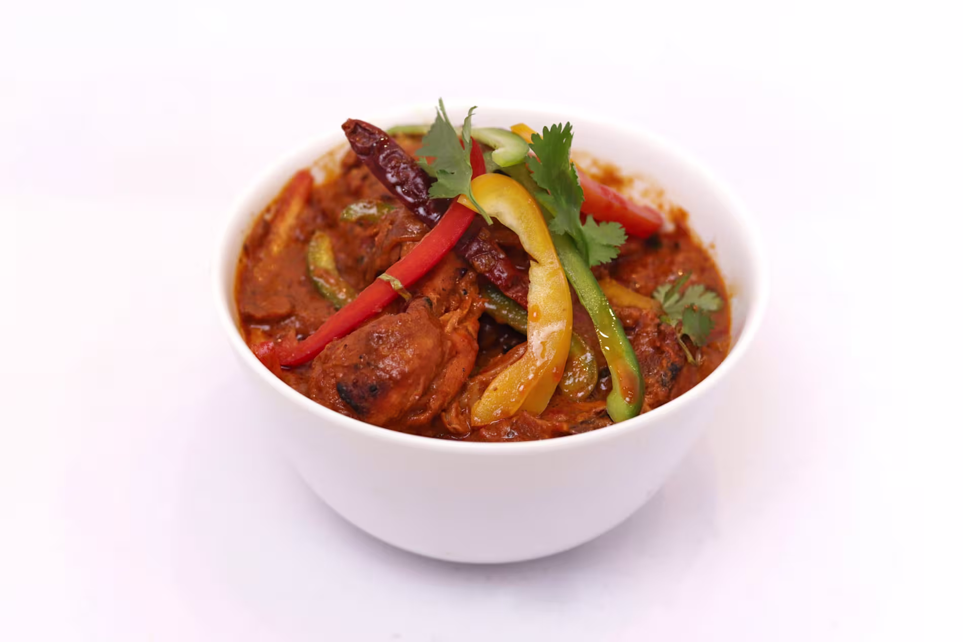 A white bowl filled with spicy curry, featuring chicken pieces, bell pepper strips, dried chili, and fresh cilantro garnish on top.