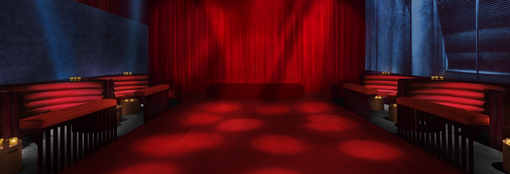 Sala de Mística, con luces rojas, cortinas elegantes y sofás modernos, creando un ambiente sofisticado y exclusivo para eventos nocturnos.