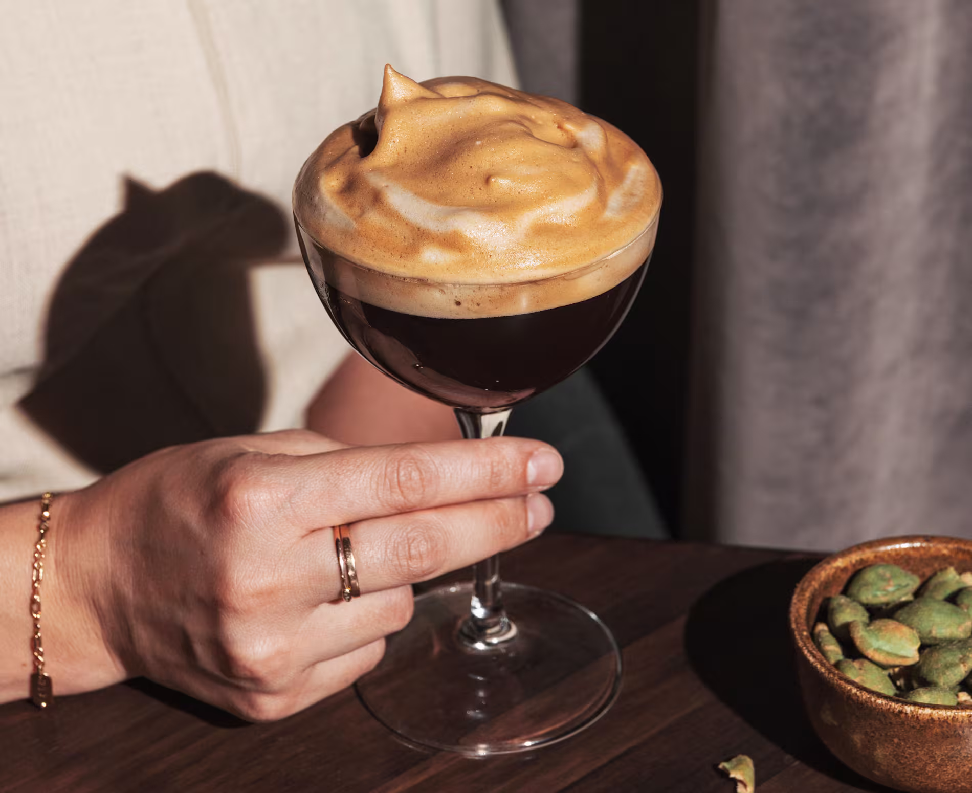 The Bar | Sips - Negroni - Primer plano de un vaso corto sobre una mesa de mármol negro con un cóctel rojo y un gran cubo de hielo esférico en su interior.