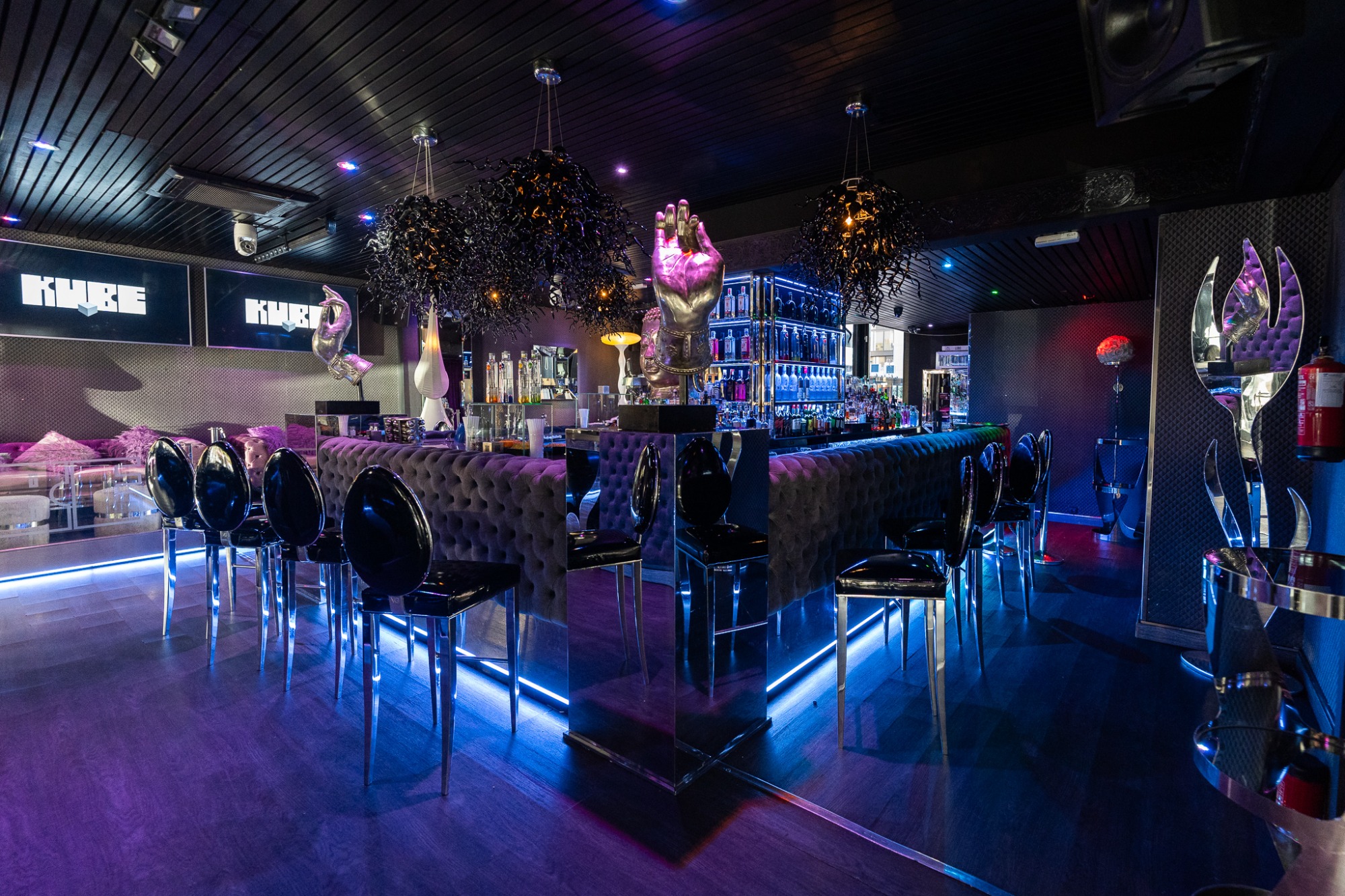 Interior moderno y elegante del bar KUBE, con iluminación azul vibrante, una barra sofisticada y decoración contemporánea perfecta para noches exclusivas.