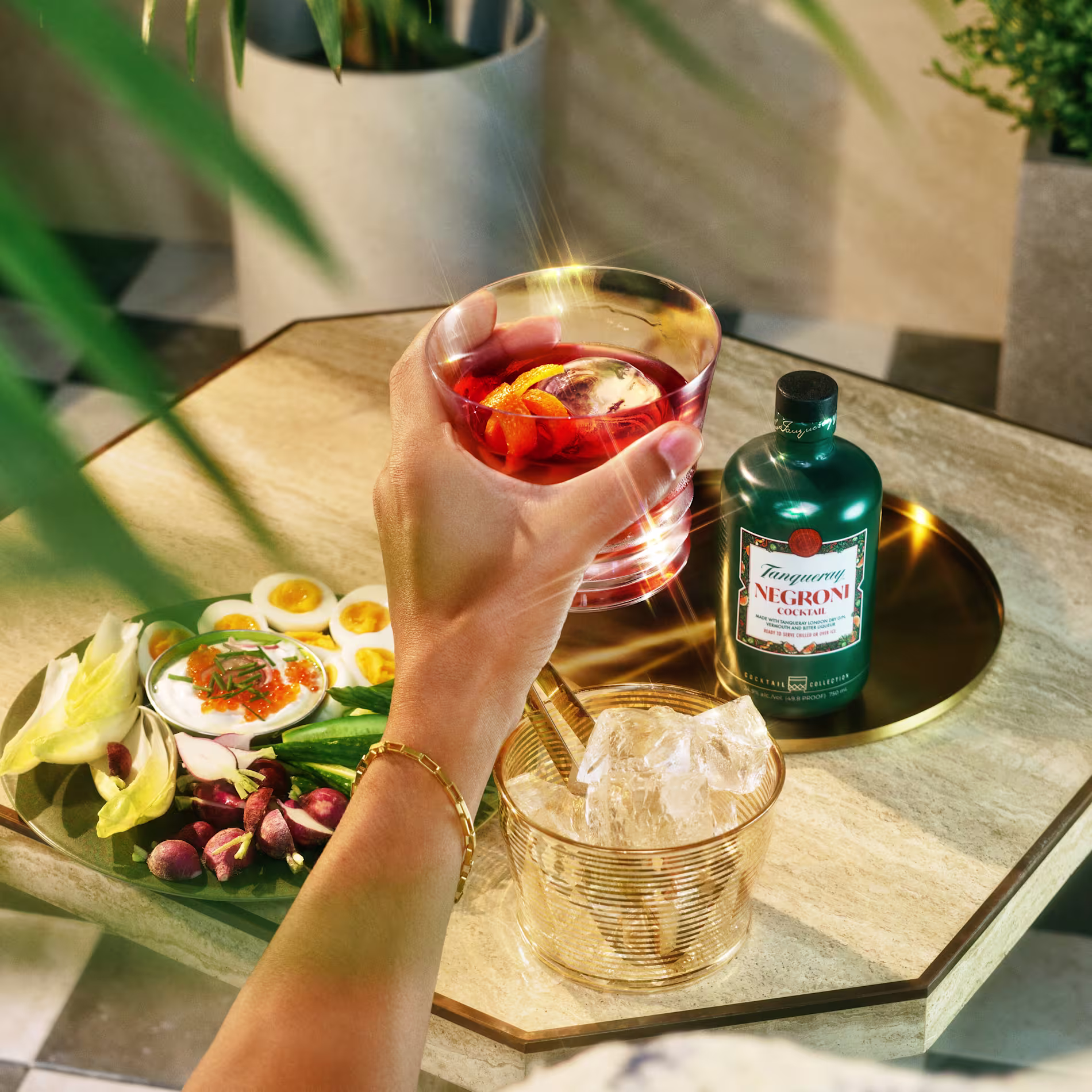 Tanqueray Negroni cocktail glass in hand with bottle on table with ice bucket.
