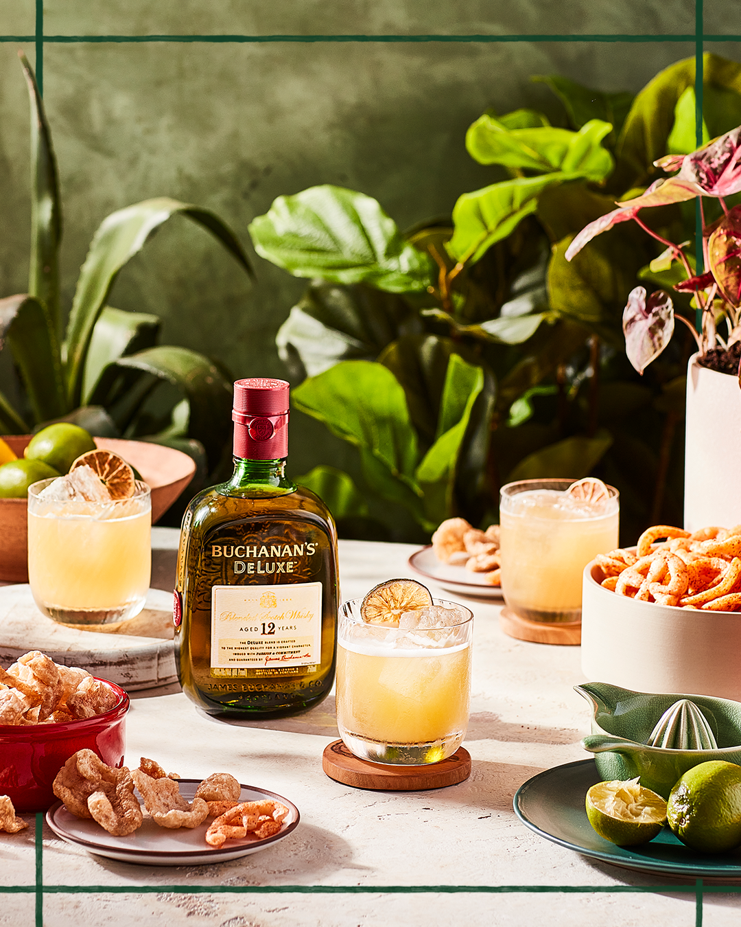 Buchanan's Penicillin Cocktail on a table surrounded by garnishes, plants and a bottle of Buchanans dry aged 12 years old Whisky