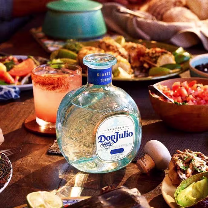 Don Julio Blanco Tequila bottle on a dinner table with a pink cocktail, tacos, salsa, and assorted Mexican food