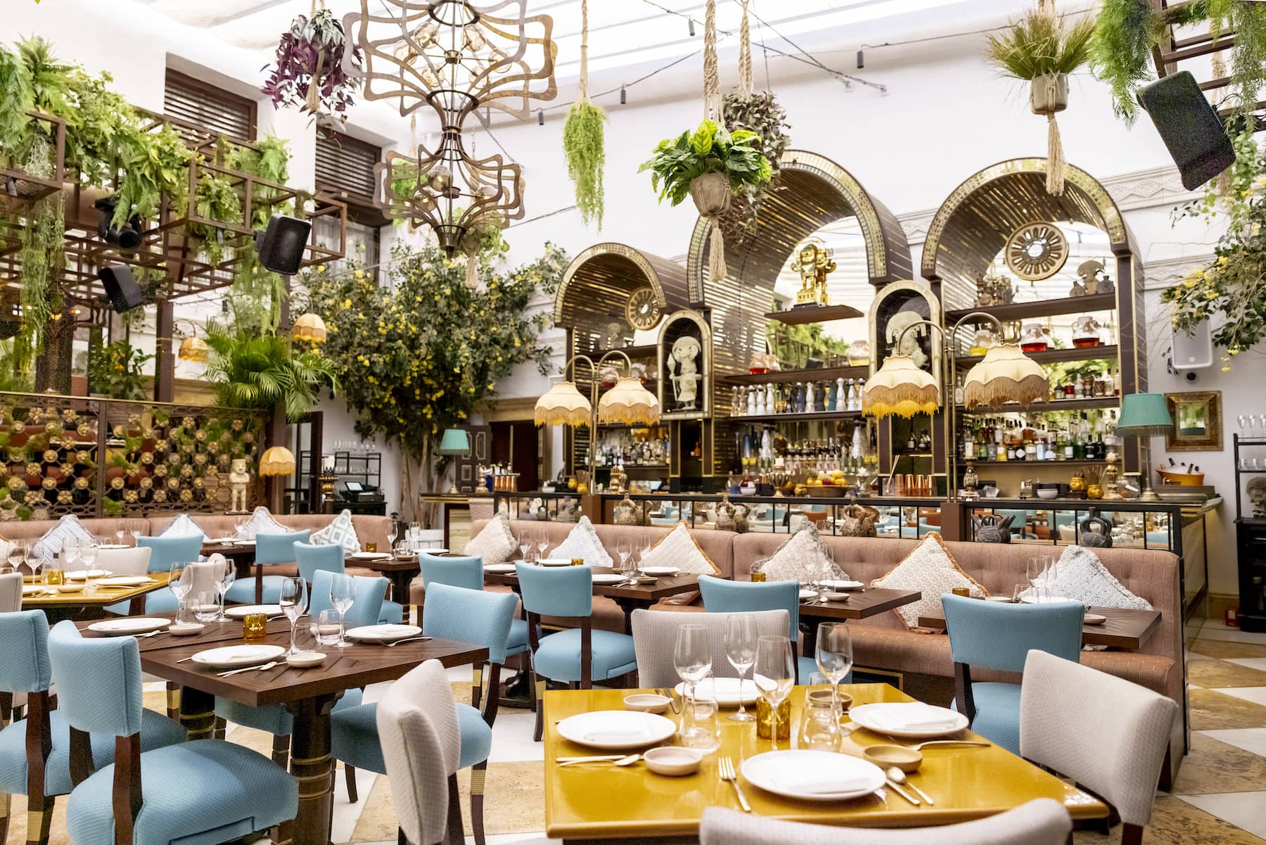COYA Marbella, una atmósfera exótica con exuberantes plantas colgantes, mobiliario colorido y detalles dorados que crean un ambiente sofisticado.