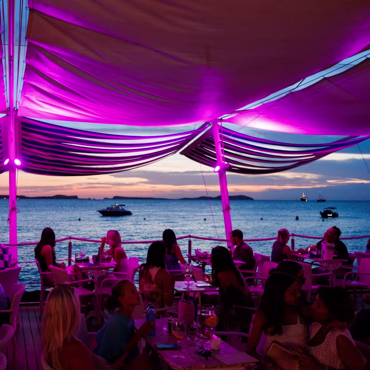 Terraza de Café del Mar en Ibiza, con vistas al mar al atardecer, luces púrpuras y ambiente relajado para disfrutar de cócteles únicos.