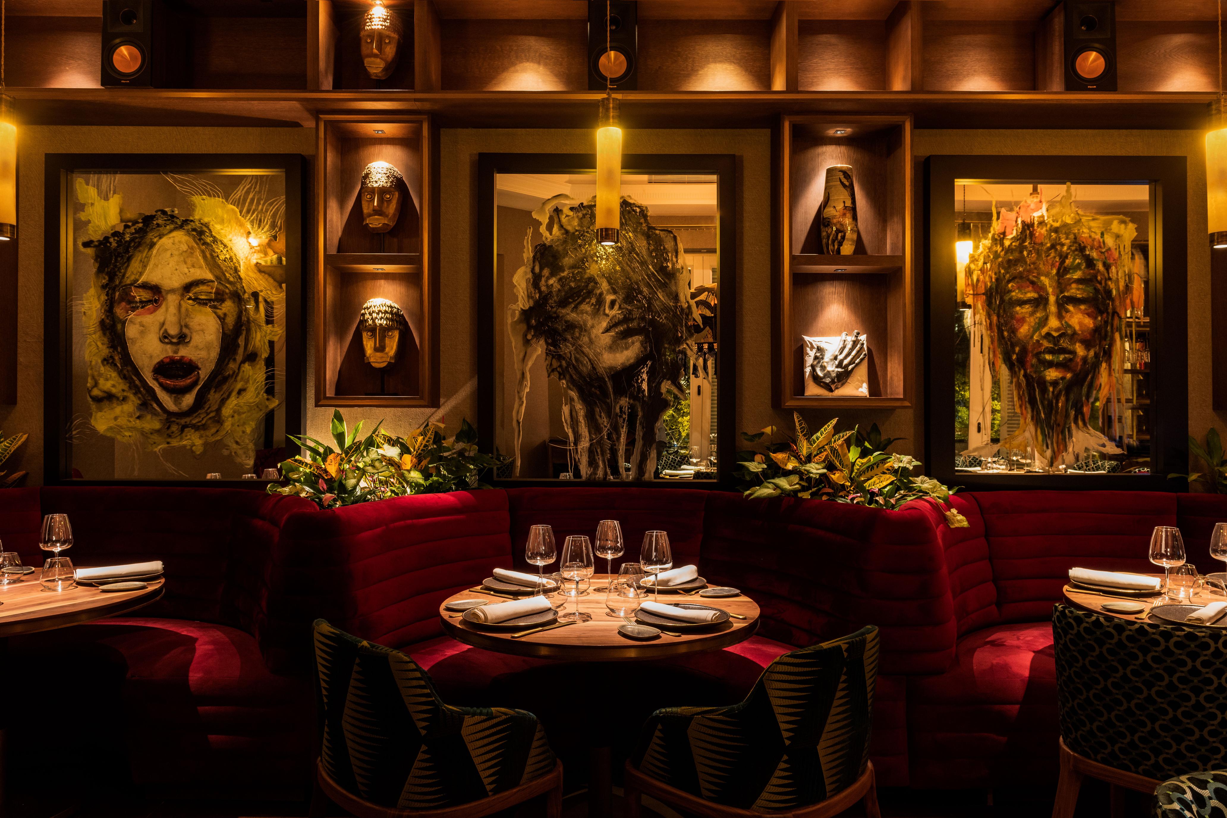 The Bar | ABYA - Vista del interior del restaurante ABYA con sofás rojos, mesas preparadas y obras de arte en las paredes.