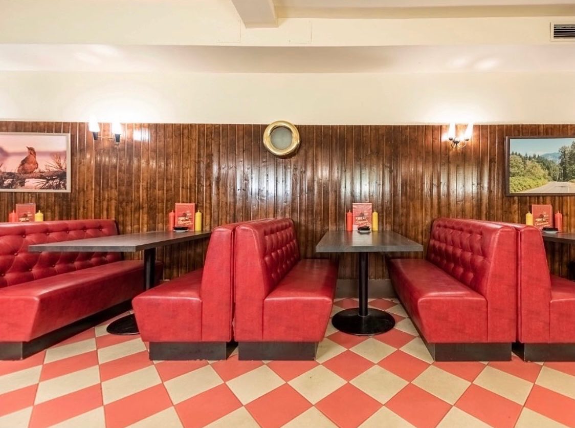 Estupenda Café Bar es un acogedor local estilo diner americano con cabinas rojas, paredes de madera y suelo de baldosas retro