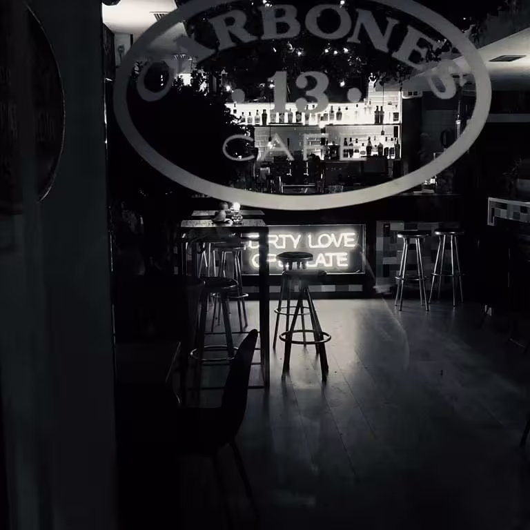 Vista en blanco y negro de Carbones 13, un lugar íntimo con luces de neón que invitan a disfrutar de buena música, amor y chocolate.