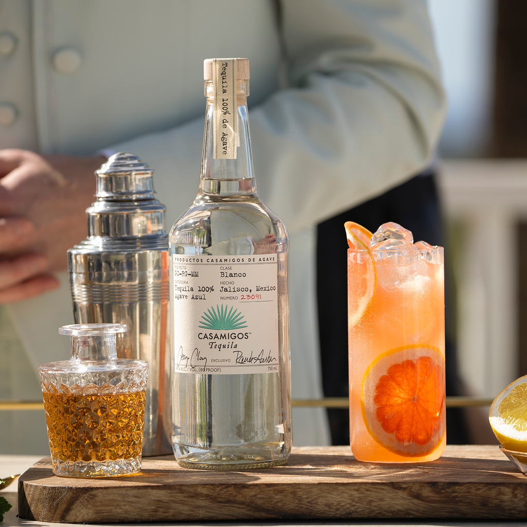 Casamigos Tequila Blanco bottle with a grapefruit cocktail, fresh lemon slices, and bar tools on an outdoor bar
