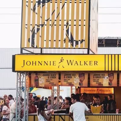 Ambiente festival diurno con stand 'Johnnie Walker'.