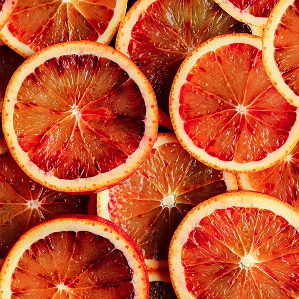 Close-up of overlapping slices of blood oranges, showing their deep red and orange hues and textured surfaces.