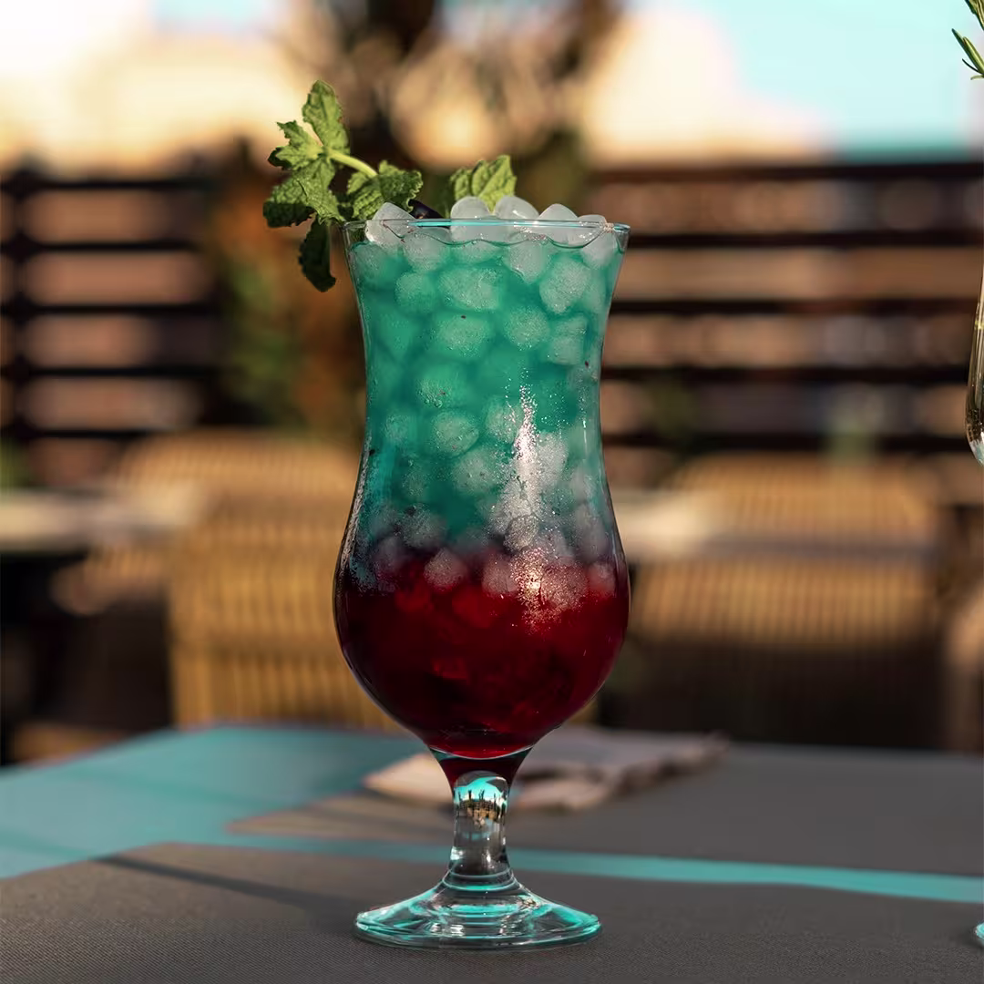 Keyzen: Cóctel refrescante en copa alta, tonos azul y rojo, decorado con menta, ideal para disfrutar al aire libre.