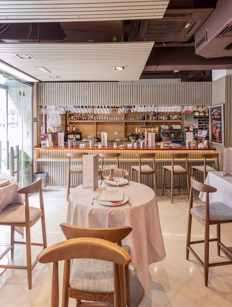 El Barril de Recoletos muestra un diseño moderno con barra de madera, copas colgantes y mesas dispuestas con elegancia y luminosidad.