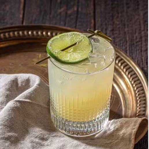A margarita cocktail is placed on a metal serving tray next to a cotton rag.