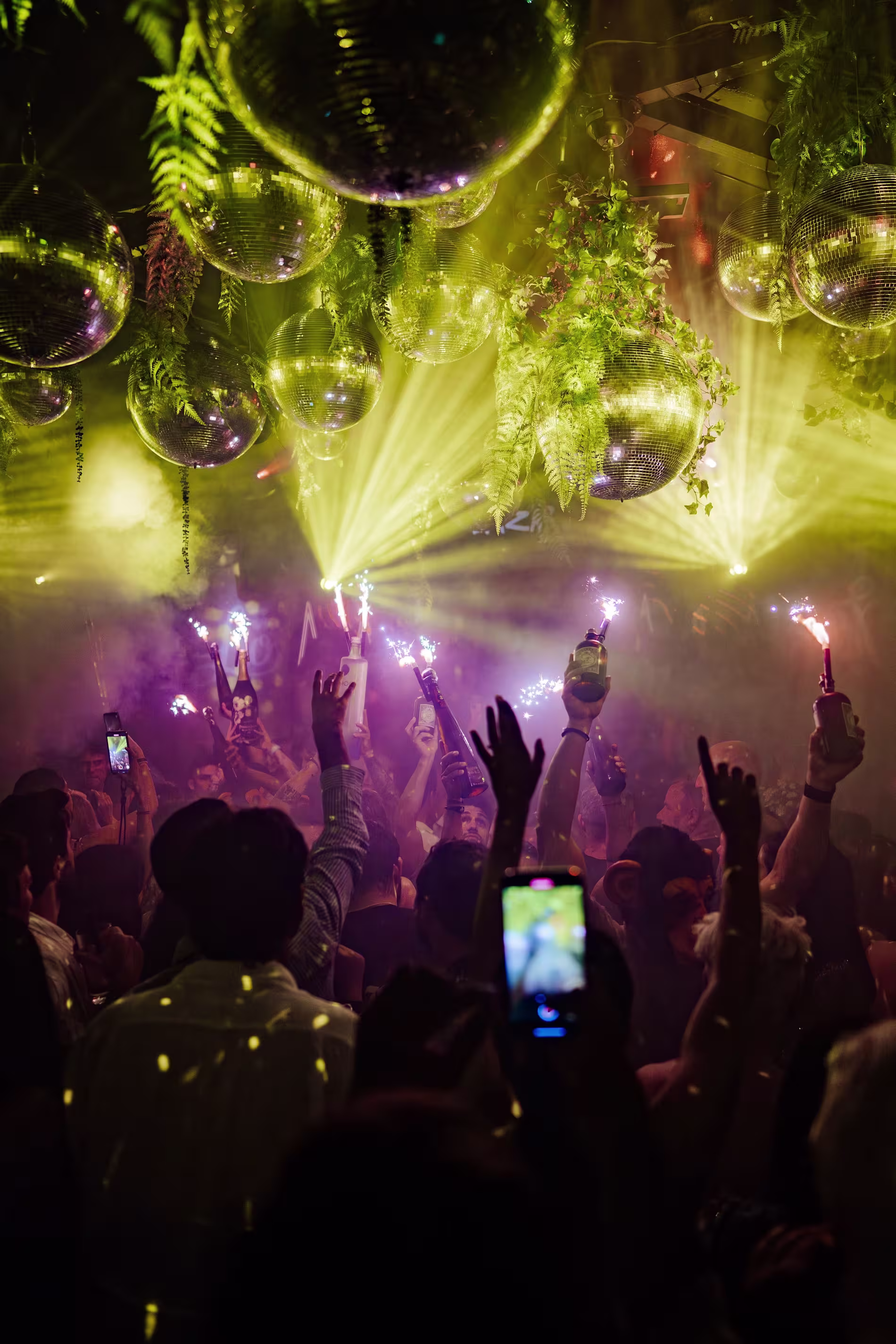 Fiesta en Lío Ibiza, con bolas de discoteca brillantes, luces en tonos amarillos y verdes, y una multitud animada disfrutando de un espectáculo.