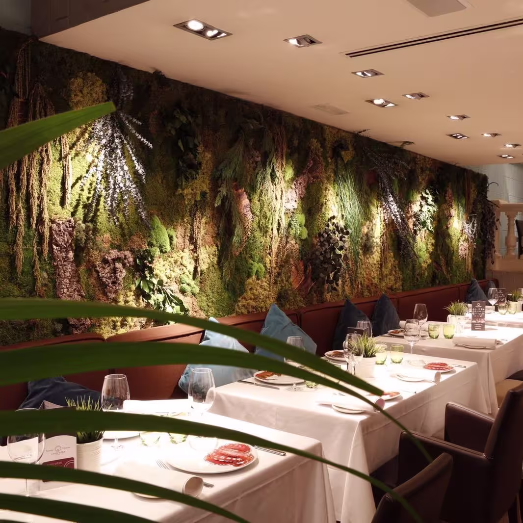 Un comedor lleno de encanto en El Barril de Orense, con un impresionante muro vegetal, iluminación tenue y mesas elegantemente preparadas.