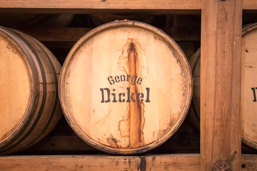 A wooden barrel with George Dickel stenciled on it, stored on a wooden rack among other barrels.