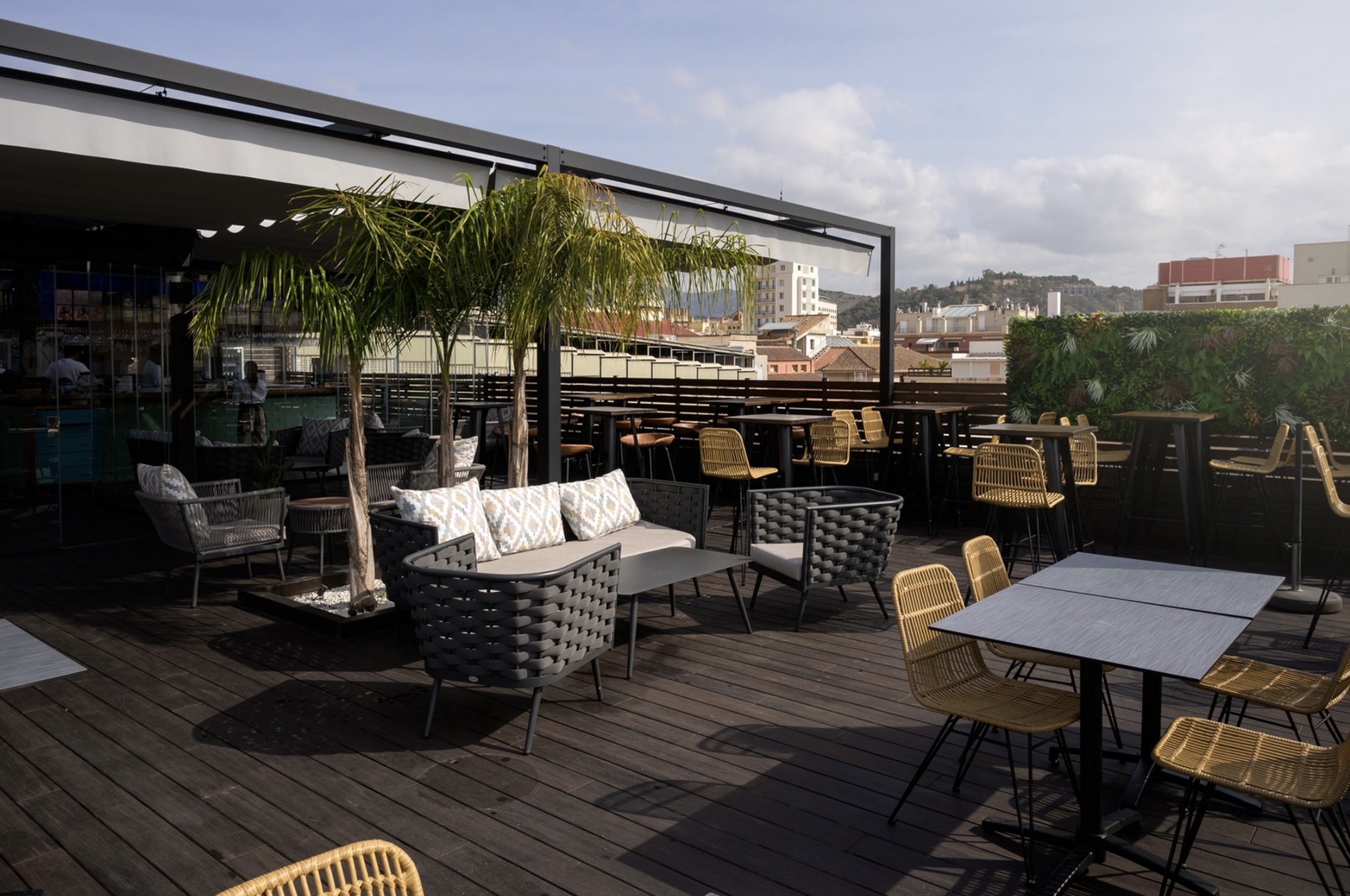 Terraza de Keyzen, con mobiliario moderno de ratán y metal, mesas elegantes, decoración vegetal y vistas panorámicas de la ciudad.