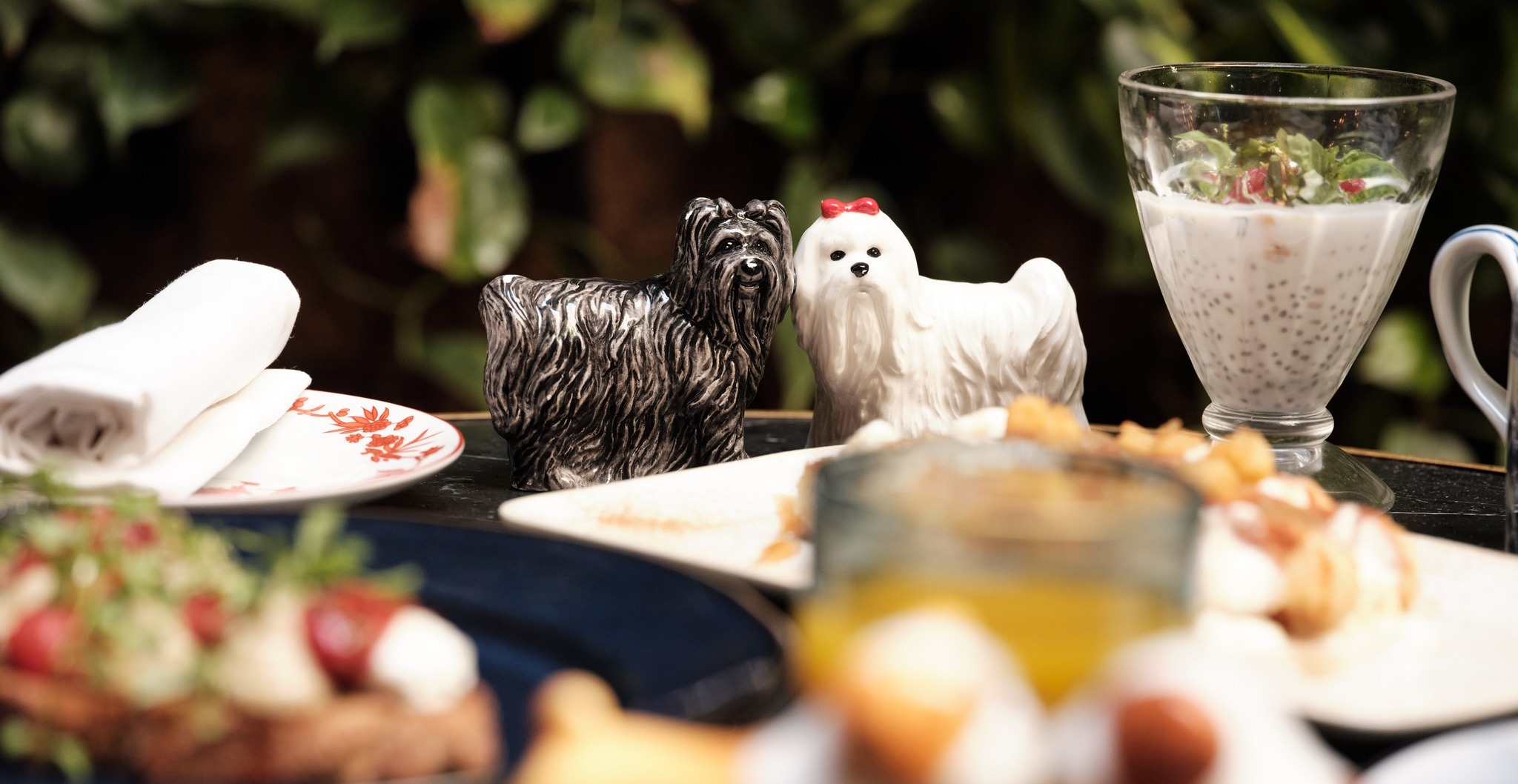 Mesa en Contraban con detalles únicos como figuras de perros decorativos, platos elaborados y un ambiente acogedor rodeado de vegetación.