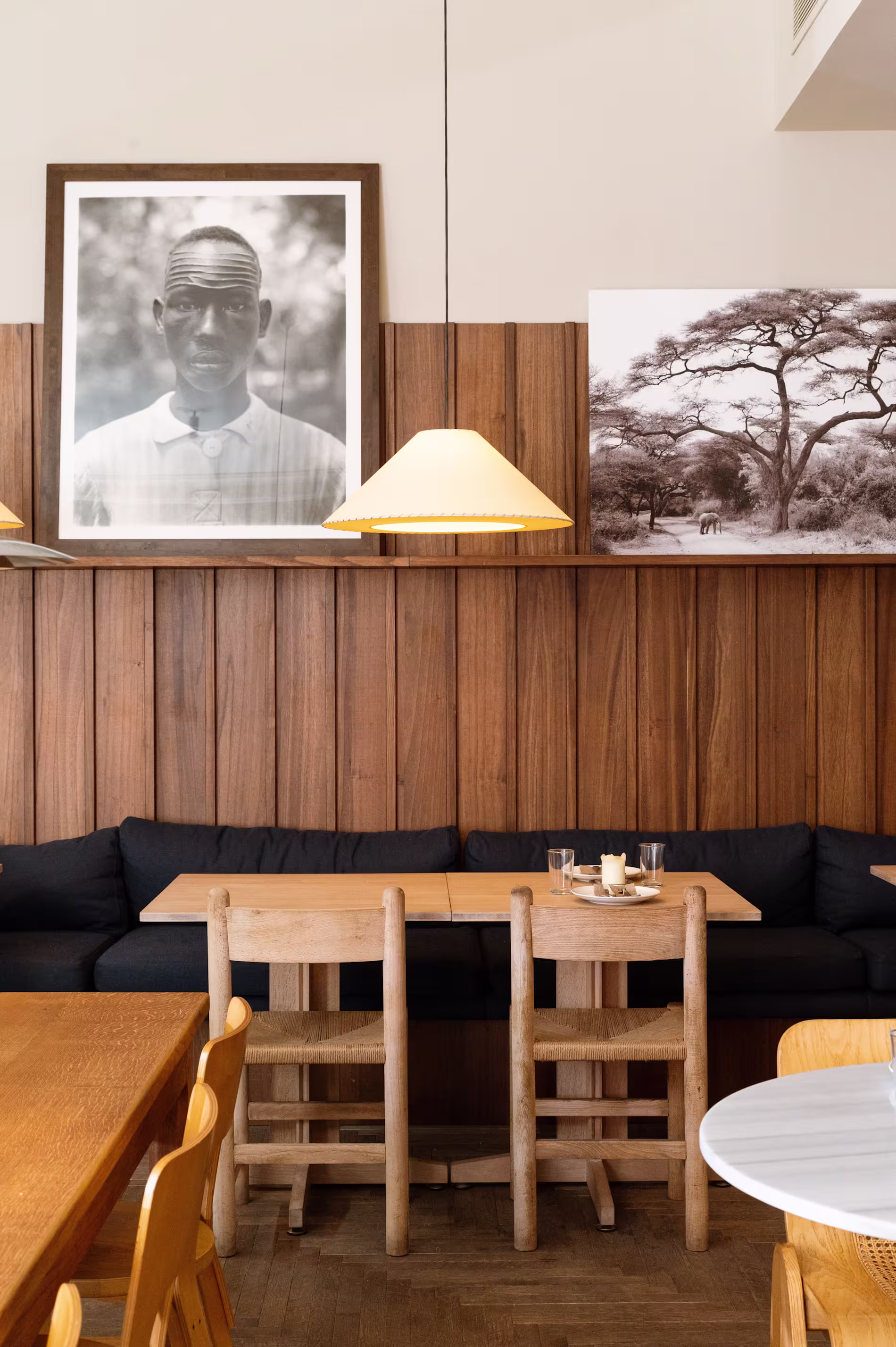 Una mesa acogedora en Bar Bauma con sillas de madera, fondo de paneles de madera, fotografías en blanco y negro y una iluminación cálida.
