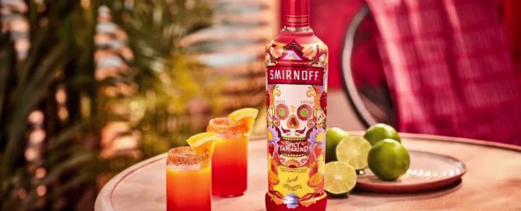 La imagen muestra una botella de Smirnoff Spicy Tamarind y dos vasos rellenos con cócteles preparados con dicho destilado junto a un plato con cinco frutas.