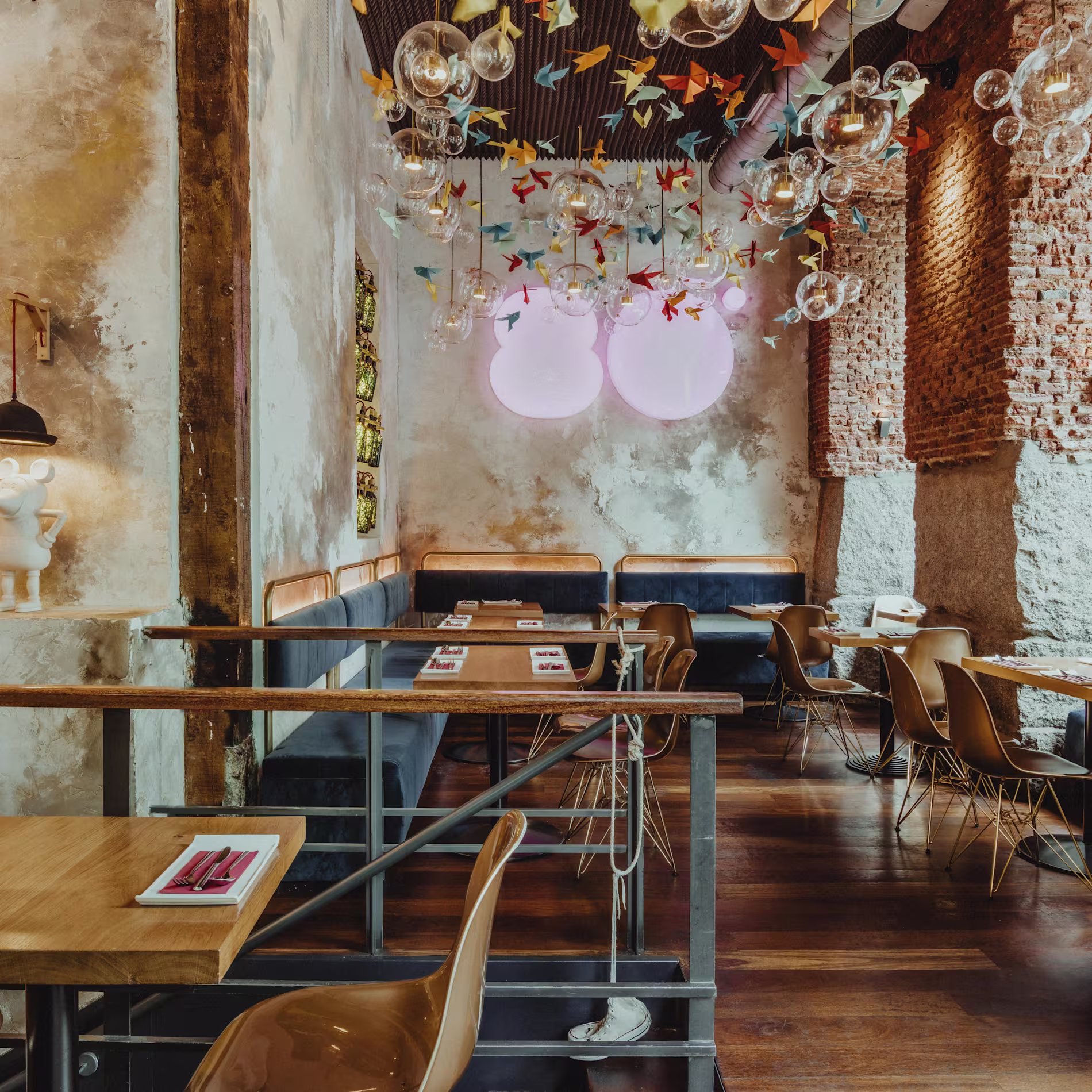 Interior de Ochenta Grados Malasaña con muros de ladrillo visto, lámparas de burbujas, grullas de papel y mesas de madera con estilo industrial y artístico.