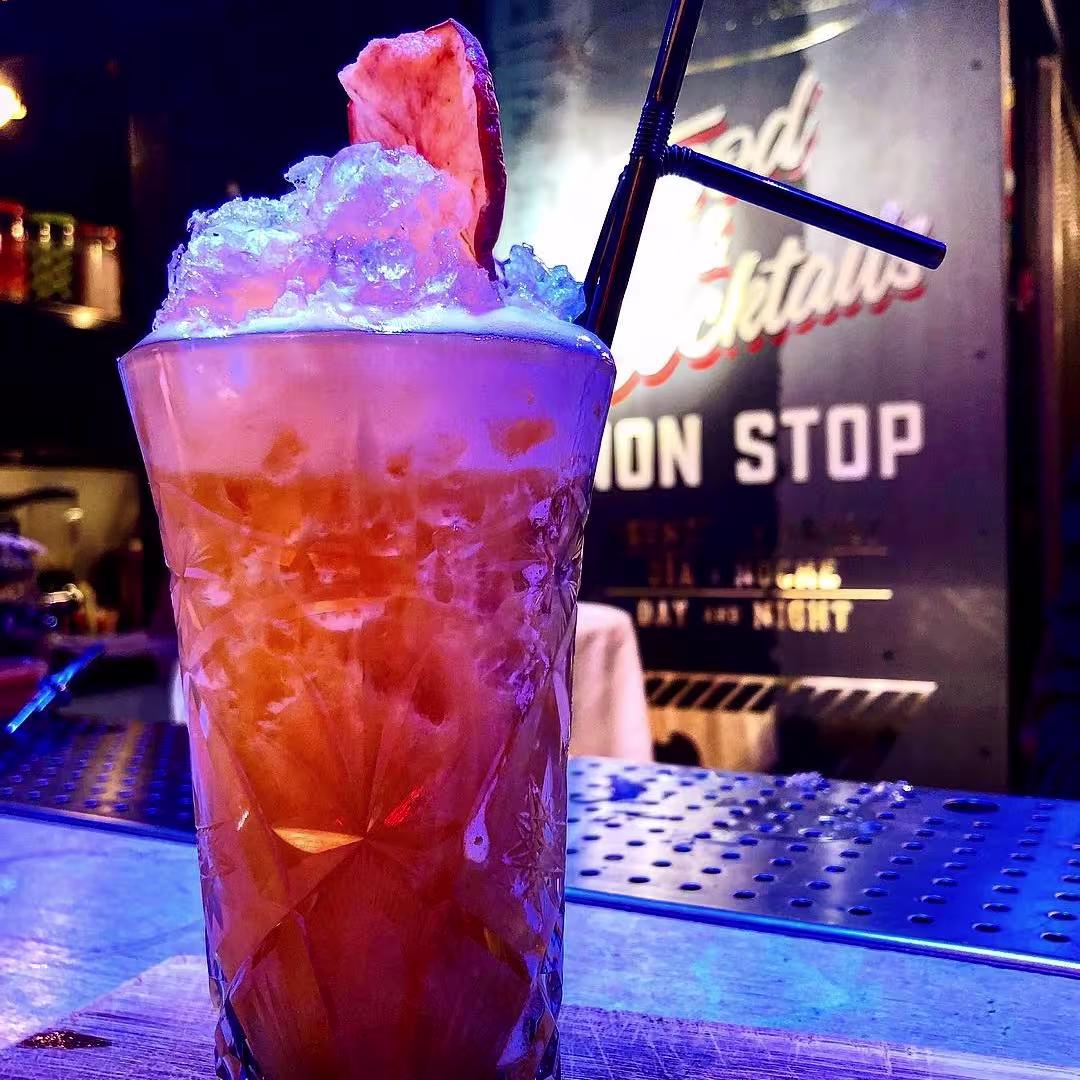 Antigua Cigarrería: Cóctel vibrante servido en vaso tallado con hielo picado, decorado con fruta deshidratada y fondo retro.