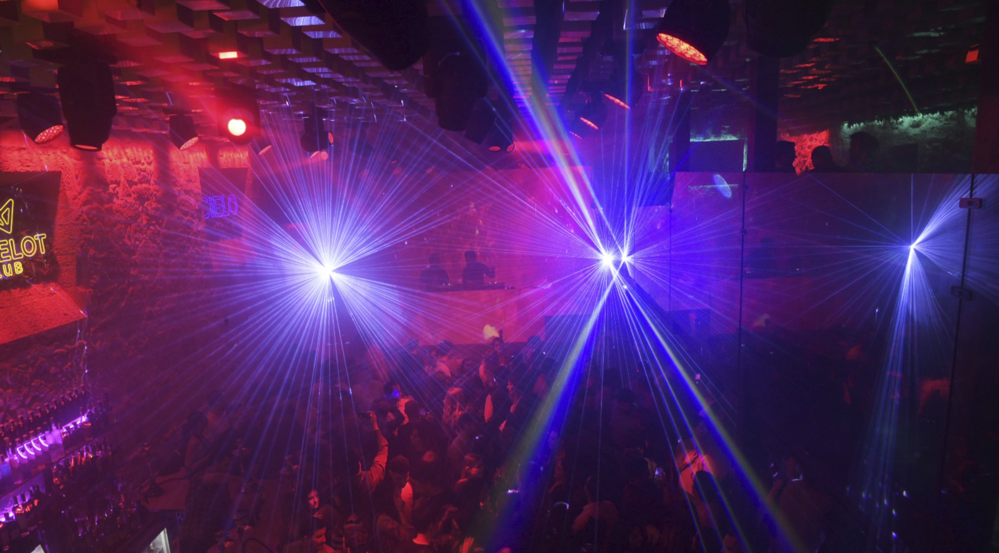 Espectáculo de luces láser en Camelot Club con ambiente vibrante, DJ en cabina y asistentes disfrutando de la música