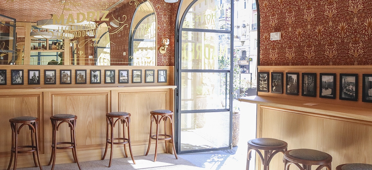 Castizo Alcalá-Canalejas, un espacio cálido con paredes decoradas, taburetes de madera y ventanales que conectan con el encanto de Madrid.