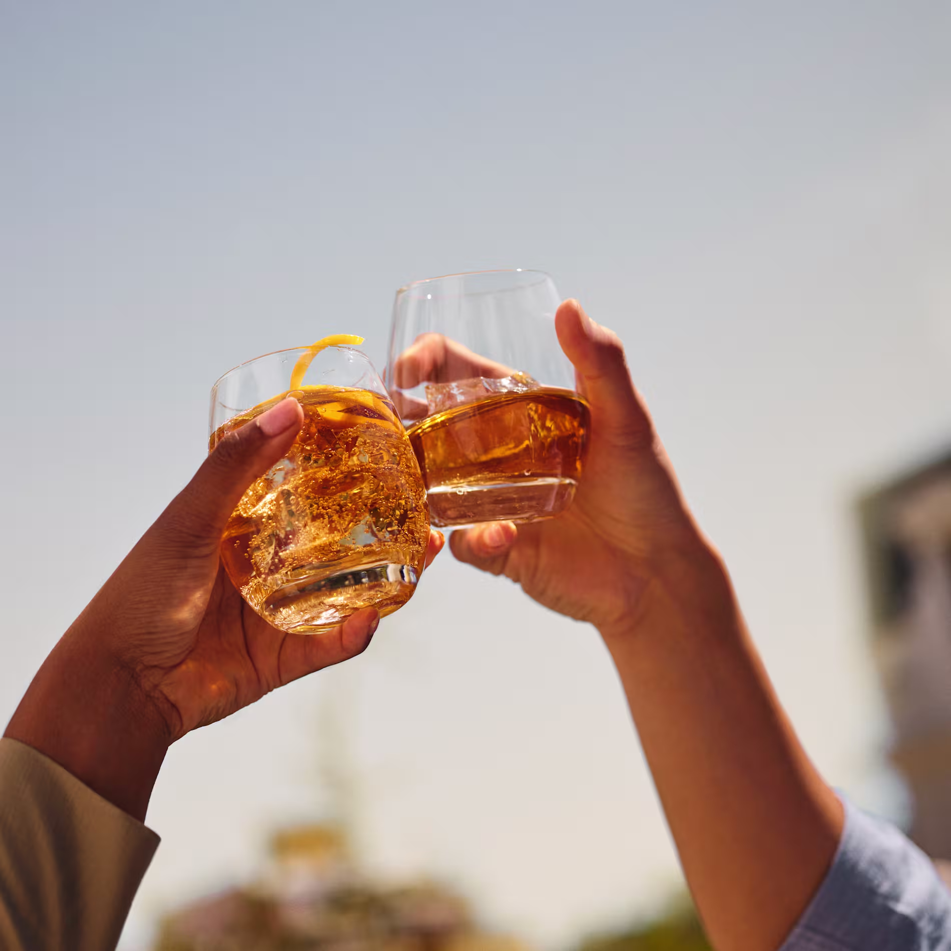 Dos vasos tintinean con whisky Old Parr en un entorno al aire libre iluminado por el sol.
