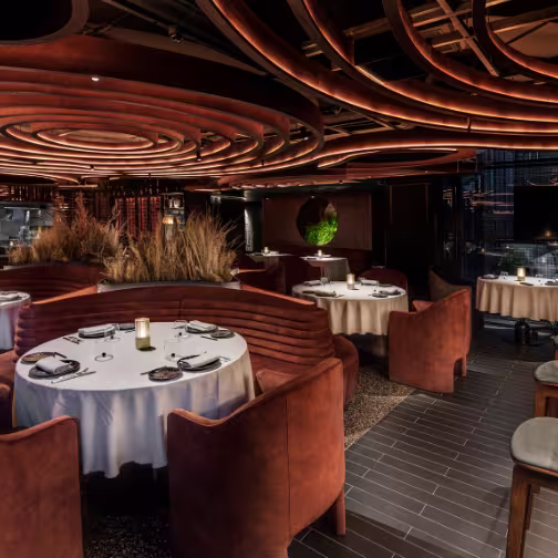 Interior de LEÑA, con diseño moderno, mesas elegantes y detalles de iluminación cálida que crean un ambiente sofisticado.